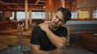 © Krakenimages.com - Young hispanic man in hotel room holding shoulder in discomfort indicating back pain with stylish interior decor lighting and furniture as background contrasting his pained expression