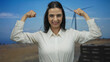 © Krakenimages.com - Young hispanic woman in white shirt outdoor by windmill field making strong gesture with arms against blue sky portraying empowerment and sustainability in natural setting