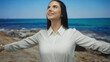 © Krakenimages.com - Woman enjoying sun at seaside with outstretched arms wearing white shirt under blue sky on rocky beach summer holiday travel outdoors peaceful serene scene
