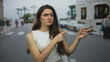 © Krakenimages.com - Hispanic teenage woman wearing white crop top finger pointing to object on busy city street crosswalk; uncertainty.