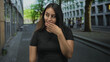© Krakenimages.com - Young hispanic woman places hand on chest on city street wearing black tshirt near urban buildings and tree lined pavement; confidence.