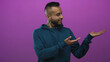 © Krakenimages.com - Young hispanic man smiling and pointing to open palm in purple studio wearing teal hoodie and ear gauge; friendly.