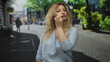 © Krakenimages.com - Woman touches face with hand on city street wearing light blue blouse and loose blonde hair, gesturing with open palm toward camera; confidence.