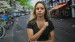 © Krakenimages.com - Woman with fist to chest on a city street, wearing black v neck tee and crossing one arm across waist; concerned reflection.