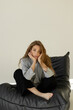 © Liudmyla - Young woman sitting on sofa. Relaxed pose, natural light, soft aesthetic, lifestyle and home comfort mood.