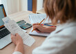 © Soloviova Liudmyla - Woman checking paper bills while calculating expenses at home. Over-shoulder view of pencil and calculator. Home budget, smart money management and personal finance planning concept