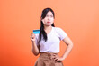 © Ajab - A pensive woman holding a credit card while looking skeptically, suggesting uncertainty or concern about a financial transaction, isolated on orange background.