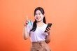 © Ajab - Young woman holding a credit card and a mobile phone, smiling happily, ready for online shopping. isolated on orange background