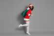 © New Africa - Beautiful woman in Mrs Claus costume with sack on gray background. Christmas season