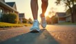 © Viktor - Person walks on suburban street in white sneakers. Legs moving forward on road at sunset. Warm sunlight illuminates houses, green lawns, trees in background.
