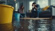 © Rifqi - Close-up flooded floor and bucket with desperate couple in background. Concept for home insurance, disaster recovery and emergency services