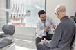 © Seventyfour - Middle Eastern male dentist explaining dental procedure to senior Caucasian man using dental model in modern dental office, both seated and engaged in consultation