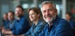 © Maryna - Senior man with grey beard smiles looking forward. Group of diverse men sit at tables in class. Adults attend seminar learning new skills for better job.