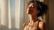 © mila103 - A young woman sits peacefully by a window basking in the warm morning sunlight. She closes her eyes and breathes deeply embracing a moment of calm and mindfulness.