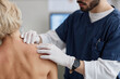 © Seventyfour - Caucasian middle aged woman sitting while male healthcare professional examining skin on back during dermatology appointment, doctor wearing gloves and medical uniform