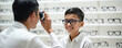 © Maryna - Boy smiles while selecting eyeglasses in optic store. Optometrist measures vision with device. Child on eye exam for vision correction. Eyewear medical healthcare concept.