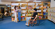 © Raushan_films - Indian young adult man sitting wheel chair take part group study speak share new ideas indoor gen z pupil teen girl boy hold book talk have fun joy library college place