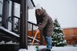 © looking2thesky - A young woman actively shovels snow with a shovel and broom in her snowy yard. Authentic winter chore captured with natural energy and seasonal realism