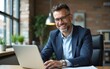© lan - Portrait of a smiling businessman working on his laptop in the office. A middle aged business man is sitting at a table with his computer. High quality