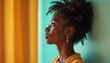 © Vadym - Side profile of a young Black woman. She looks upwards with a thoughtful expression. She wears a yellow sweater and earrings. The backdrop is a mix of yellow and blue colors.