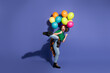 © deagreez - Young girl with colorful balloons jumps in the air smiling against purple backdrop to convey fun celebration fashion carefree lifestyle moments