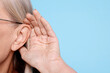 © New Africa - Senior woman showing hand to ear gesture on light blue background, closeup. Space for text
