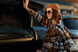 © SHOTPRIME STUDIO - Woman with beanie and sunglasses smiling while loading shopping into a car trunk at golden hour, candid lifestyle moment in plaid coat with authenticity, mindful living and emotional storytelling.