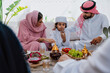 © oneinchpunch - Emirati family at home. Muslim family sharing tea and traditional sweets on a rustic table outdoors, celebrating culture, warmth and togetherness