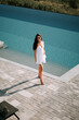 © Darius - Young woman enjoying a sunny day by the poolside in a stylish white dress