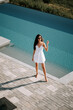 © Darius - Young woman in a white dress enjoying a sunny day by a tranquil pool