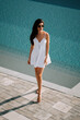 © Darius - Young woman walks by pool in summer dress enjoying sunny day outdoors