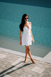 © Darius - Woman in white dress walking by the poolside on a sunny day at a luxury resort