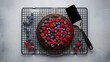© Wool World - Delicious homemade chocolate cake with fresh raspberries and blueberries on a cooling rack.