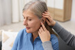 © New Africa - Woman putting hearing aid into her mother's ear at home, closeup
