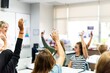 © Rawpixel.com - Students in classroom raising hands, engaging in learning. Diverse group of students participating. Classroom setting with teacher guiding students. Students raising hands and asking questions.