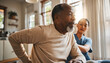 © SYATRI RAWU - Elderly African American man with lower back pain receiving supportive care from a compassionate female nurse during an in-home medical visit