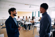 © Maskot - Smiling male teacher talking with teenage student while standing in high school classroom
