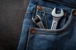 © wilson - Close-up of a mechanic's jeans pocket with tools and wrenches arranged on dark surface, celebrating mechanics day with copy space for text or logo design.