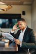 © Maskot - Concentrated male lawyer reading document while sitting at table in office