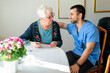 © Maskot - Smiling male home caregiver sitting with arm around elderly woman taking pills