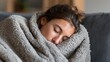 © mila103 - A young woman is sleeping soundly on a couch wrapped in a fluffy blanket. The setting is warm and inviting perfect for a restful afternoon nap.