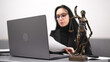 © wedmoments.stock - A female lawyer reviews legal documents at a modern office desk with a statue of the goddess of justice and a laptop symbolizing fairness and professionalism.