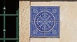 © andi - A square of ornate blue tiles adorns a sunlit beige wall next to a green window