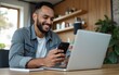 © James - Cheerful male professional holding smart phone while using laptop on table at home. High quality