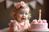 Sweet baby girl celebrates first birthday. She smiles happily near pink cake with one candle. Kid wears dress flower headband. Party decorations indoors.