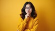 © Pete - Thoughtful asian girl in glasses looks up. Pensive young woman in yellow sweater thinking. Intelligent student doubts, considers question. Lady finds solution against solid background. Smart.