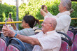 © luciano - Group of three seniors enjoying a sightseeing tour on an open-top bus. They sit together listening to audio guides through earphones while take photos with smartphone.