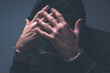 © Bits and Splits - Low-key portrait of a hooded criminal with hands raised to an obscured face, handcuffs visible and dramatic shadows emphasizing tension and guilt.