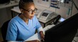 © Eve - Dedicated African-American female doctor working late on computer in a modern clinic or hospital office, reviewing patient data for telemedicine and health.