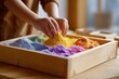 © Iryna - Child's hands playing with colorful sand in a wooden tray